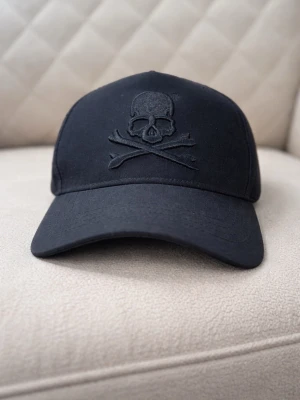 Philipp Plein keps  - Säljer en svart keps från Philipp Plein med broderad dödskalle och korslagda ben på framsidan. På sidan sitter en metallbricka med märkets logga. Kepsen har böjd skärm och justerbar passform. Bra kondition, skickas inom 1 dag