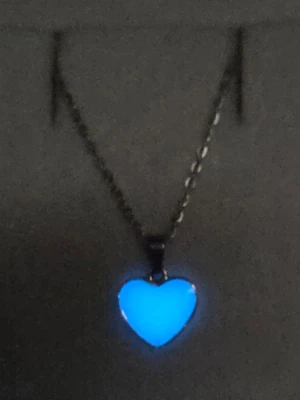 Halsband med självlysande hjärthänge - Snyggt halsband med ett hjärtformat hänge som lyser i blått i mörker och är ljusgul/svagt glittrig i dagsljus. Kedjan är i rostfritt stål och hänget har en slät, glansig yta. Perfekt för dig som gillar unika accessoarer med cool effekt. Hjärtat började lysa i mörkare omgivning efter att jag tog kort på det i fönstret. (Vanligt dagsljus, även molnigt väder, aktiverar skenet i hänget). Tål vatten & missfärgas inte. Lång livslängd. 