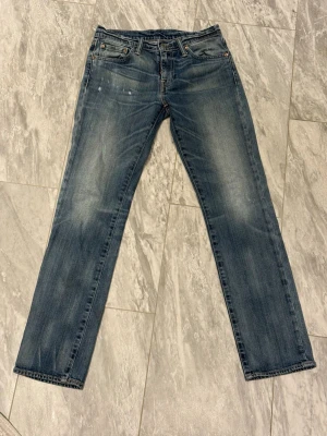 Levi's blå raka jeans - Klassiska blå jeans från Levi's med rak passform och fem fickor. Jeansen har en snygg tvättad look med lätt slitning på låren och knäna. Tillverkade i slitstark denim med detaljer som nitar och läderpatch bak i midjan.
