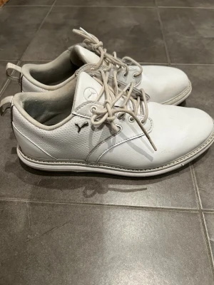Vita golfskor från Puma i läder, stl 39 - Säljer ett par vita golfskor från Puma med klassisk låg profil och snörning, jättefint begagnat skick, innersula, yttersula och häl helt intakt. Skorna är tillverkade i slätt läder med diskret Puma-logga på sidan och tungan. Perfekta för en clean och stilren look på golfbanan⛳️.