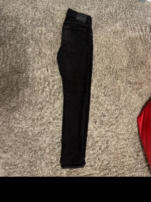 Svarta  jeans från Lee - Säljer ett par svarta  jeans från Lee med klassisk femficksdesign och hög midja. Jeansen har Lee-logga på bakfickan och patch bak i midjan. Tillverkade i stretchigt denimtyg för en bekväm passform. Perfekta till alla outfits!