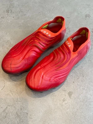 Adidas Copa Sense+ Elite röda fotbollsskor FG - Säljer ett par Adidas Copa Sense+ Elite fotbollsskor i rött och vita detaljer med en vit sula. Skorna har en strömlinjeformad design utan snörning och är tillverkade i kängeruläder för bästa bollkontroll och känsla . Perfekta för dig som vill sticka ut på planen fast forfarande vill ha en mjuk och skön känsla. Dobbarna är Fg som rekommenderas att spela på naturgräs och inte konstgräs. 