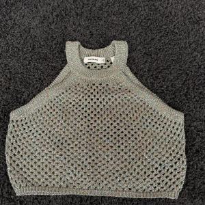 Glittrig stickad linnetopp från Sandro - Säljer en glittrig stickad linnetopp från Sandro i silverton. Toppen är ärmlös med breda axelband och har ett hålmönster över hela plagget som ger en luftig känsla. Perfekt för dig som vill sticka ut med en unik och trendig topp.