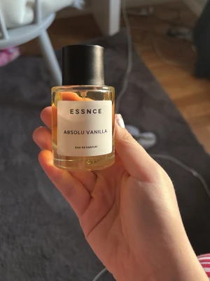 ESSNCE Absolu Vanilla parfym - En stilren parfym från ESSNCE med doften Absolu Vanilla. Flaskan är cylindrisk i genomskinligt glas med svart lock och enkel vit etikett. Innehållet är gyllengult och flaskan har en modern, minimalistisk design som passar perfekt på sminkbordet. Knappt använd, säljer då jag inte kan returnera den!