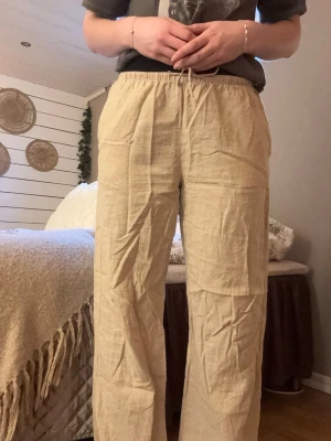 Beige linnebyxor från Gina Tricot - Beige linnebyxor från Gina Tricot med avslappnad passform och snörning i midjan. Perfekta för varma dagar, med elastisk midja och raka ben. Lätta och luftiga i materialet, passar till allt. Använda ett fåtal gånger. Bra längd - jag är 167 cm.