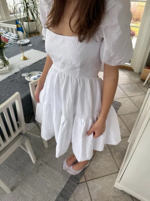 Student klänning från Bardot - Supersöt vit kortklänning med puffärmar, volangkjol och fint mönster. Klänningen är från Bardot och är knappt använd. Inga defekter. Perfekt till student eller sommarens alla tillfällen.