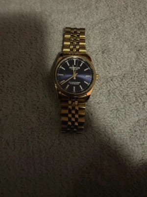 Guldfärgad Koloss klocka med blå urtavla - Stilren klocka från Koloss med guldfärgad länk och mörkblå urtavla. Klassisk design med tydliga index och metallarmband som ger en lyxig känsla. Perfekt accessoar för dig som vill sticka ut med en elegant look.