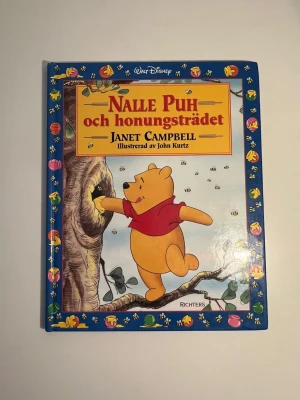 Nalle Puh och honungsträdet bok - En färgglad bilderbok med hårda pärmar, 'Nalle Puh och honungsträdet' av Janet Campbell, illustrerad av John Kurtz. Boken har klassiska Disney-illustrationer med Nalle Puh i röd tröja och många söta bilder i färg. Perfekt för dig som gillar sagor och nostalgi.