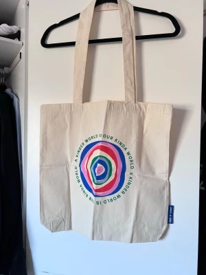 Beige tygväska från Cotton On - Säljer en beige shoppingväska från Cotton On i Australien med färgglatt cirkelmönster. Väskan har långa handtag och är perfekt till skolan eller stranden. Aldrig använd.