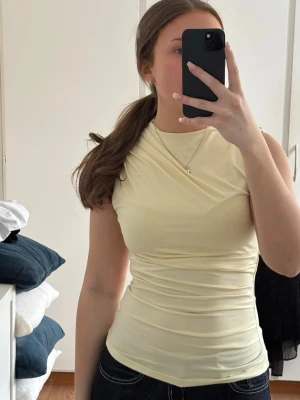 Ljusgul ärmlös topp med drapering - Snygg ljusgul, ärmlös topp från HM med snygg drapering. I storleken S, inga defekter. Toppen har en tight passform. Perfekt att styla med jeans eller kjol.💗