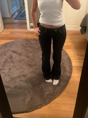 Mörkblå bootcut jeans frå - Säljer ett par mörkblå bootcut jeans från med kontrastsömmar och klassisk femficksdesign. Jeansen har låg midja och är tillverkade i ett stretchigt denimtyg som sitter snyggt på kroppen. Perfekta för en avslappnad och trendig look.