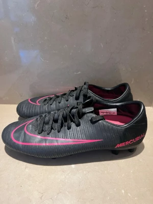 Svart Rosa Nike Mercurial fotbollsskor - Ett par använda fotbollsskor i fint skick, ett litet hål längst fram på ena skon som knappt syns. Storlek 42,5