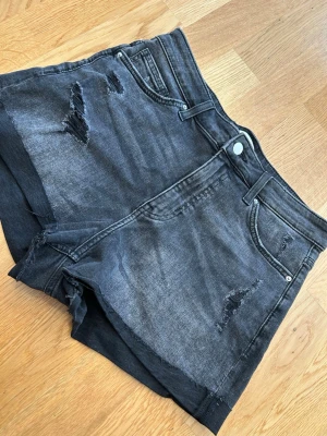 Svarta denimshorts med slitningar - Snygga svarta jeansshorts i denim med slitna detaljer och råa kanter. Klassisk femficksmodell med knapp och dragkedja framtill. Perfekta för en avslappnad och trendig look.