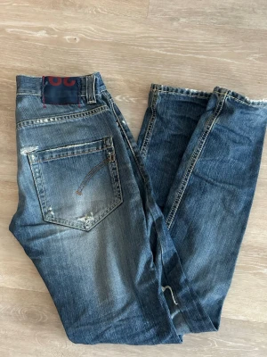 Dondup jeans 29 - Säljer ett par blå jeans från Dondup med slitningar och distressed detaljer på både fram- och baksida. Jeansen har klassisk femficksmodell, normal midja och raka ben. Snygga kontrastsömmar och patch bak i midjan. Perfekta för en avslappnad streetstil.