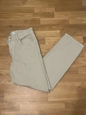 Beige Jeans från Zara - Snygga beige jeans från Zara med rak/tapered passform och klassisk design. Byxorna har knappgylf, bälteshällor och två sidofickor