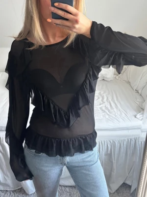 Topp med volanger - Genomskinlig blus med långa ärmar och volanger. Storlek M från MSCH Copenhagen.