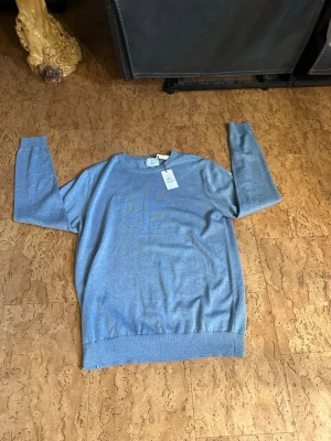Ljusblå stickad tröja från BläcK - Snygg ljusblå stickad tröja från BläcK med rund halsringning och ribbade muddar vid ärmslut och nederkant. Tröjan har en clean och enkel design som passar perfekt till jeans eller chinos. Materialet känns mjukt och bekvämt. Ny pris 599 (bara testad)