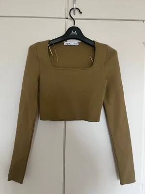 Olive green croppad topp från Zara - Trendig olive green croppad topp från Zara med lång ärm och fyrkantig urringning. Snygg och enkel design som passar perfekt till höga jeans eller kjol. Materialet känns stretchigt och bekvämt.