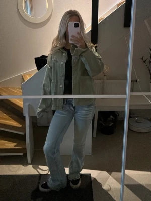ZARA - jeansjacka  - Stilren overshirt i ljusgrönt från Zara. Modellen har en avslappnad passform, två stora fickor framtill och knäppning med metallknappar. Materialet är kraftigt bomullstyg som ger en cool och trendig look. Perfekt att bära över en t-shirt för en casual vibe.