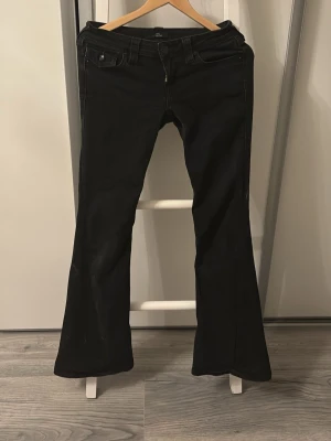 True religion jeans i modellen joey - Säljer ett par svarta bootcut jeans med snygga fickdetaljer och låg midja. Jeansen har klassisk femficksdesign, bälteshällor och dragkedja med knapp. Materialet är stretchigt för en bekväm passform och de har en lätt utsvängd siluett nedtill. Längden passar för de som är 164 - 170