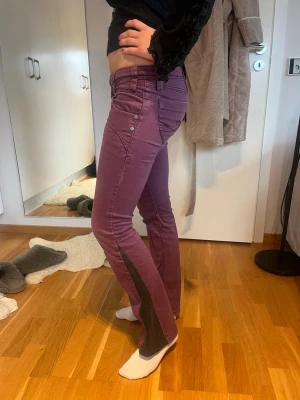 Lila bootcut jeans med svarta detaljer - Säljer dessa såååå coola jeansen som är lila och utsydda till bootcut med svart tyg. De är i jättebra skick med coola fickor både fram och bak. Midjemåttet är 38 cm rakt över och innerbenslängd 71 cm. Bara att skriva för frågor 💗💗