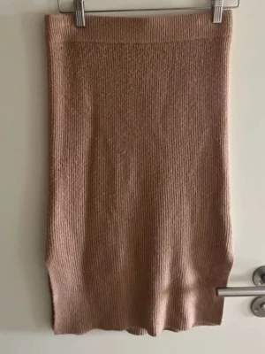 Beige stickad kjol från Donna Romina - Säljer en beige stickad kjol från Donna Romina x NA-KD. Kjolen är ribbad och har en rak, kroppsnära passform som slutar under knät. Perfekt att styla med en enkel topp eller oversized tröja.