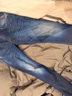 Blå jeans från Replay med tvättade detaljer - Snygga blå jeans från Replay med klassisk femficksmodell och coola tvättade detaljer. Jeansen har normal midja, dragkedjegylf och Replay-logga på fickan. Materialet är mjukt denim som sitter skönt och ger en avslappnad look. Säljes då de ej används, nypris 1499:)