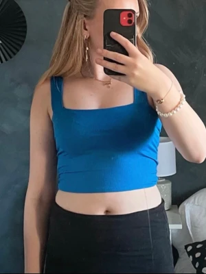 Blå croppad linnetopp - Snygg blå croppad linnetopp med breda axelband och fyrkantig ringning. Perfekt till sommaren och enkel att matcha med både jeans och kjol. Materialet känns mjukt och stretchigt för en bekväm passform.