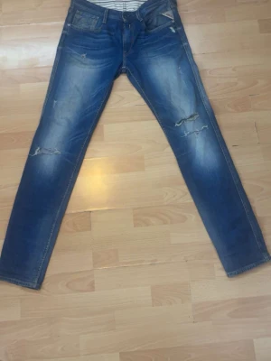 Blåa Replay jeans med slitningar  - Säljer ett par blåa Replay jeans i W32 L34 med slitningar. Jeansen har klassisk femficksdesign och dragkedjegylf. Passformen är normal Perfekta för en avslappnad och trendig look.
