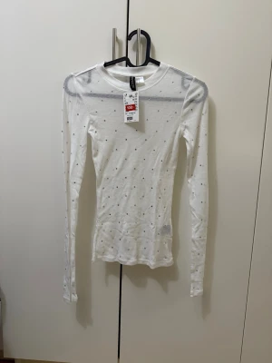 Vit mesh topp med prickar från H&M - Säljer en tunn och transparent vit mesh topp från H&M med små svarta prickar. Toppen har lång ärm och en tight passform som sitter snyggt på kroppen. Perfekt att styla lager på lager eller med ett linne under.