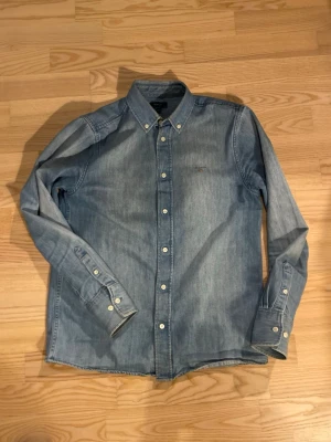 Ljusblå jeansskjorta från Gant - Säljer en klassisk ljusblå jeansskjorta från Gant i storlek 15Y, 170 cm. Jag har använt den flitigt då den sitter perfekt och är skön att bära. Perfekt till en avslappnad stil.