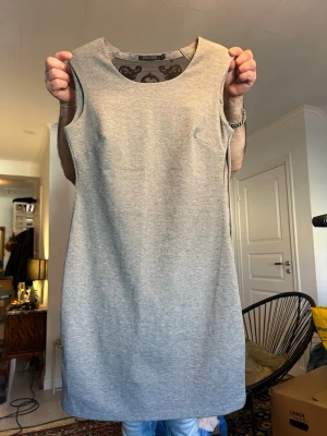 Grå ärmlös klänning med meshdetalj - Snygg grå ärmlös klänning med rund halsringning och unik meshdetalj med svart mönster i ryggen. Klänningen har en rak, enkel passform och är tillverkad i ett mjukt material som känns bekvämt mot huden. Perfekt för dig som gillar stilrena plagg med en twist.