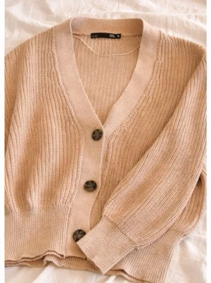 Beige stickad kofta med knappar - Mysig beige stickad kofta från Gina Tricot med tre stora knappar framtill. Koftan har v-ringning, ribbade muddar och en avslappnad passform. Perfekt att slänga över en t-shirt eller linne för en chill look.