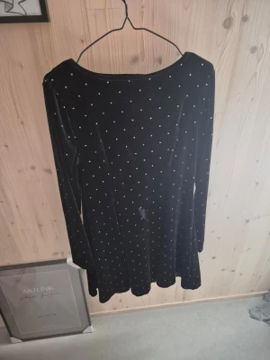 Svart sammetsklänning - Snygg svart sammetsklänning från Emery Rose med små vita prickar över hela tyget. Klänningen har lång ärm och en klassisk rund halsringning. Perfekt för dig som gillar en mjuk och bekväm känsla med lite extra stil.