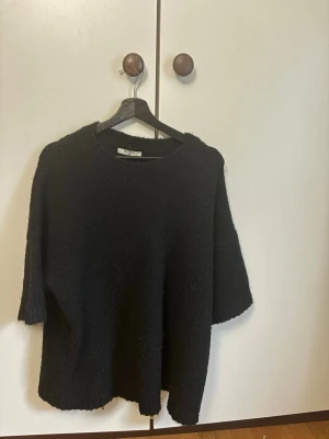 Svart stickad tröja från NA-KD - Mysig svart stickad tröja från NA-KD med rund halsringning och halvlånga ärmar. Tröjan har en avslappnad passform och är tillverkad i ett mjukt, fluffigt material som känns skönt mot huden. Perfekt för lager på lager och enkel att styla.