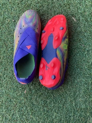 Färgglada adidas fotbollsskor - Säljer ett par adidas fotbollsskor i en färgstark mix av lila, röd, gul och grön. Skorna har ett mönstrat tyg, täckt snörning och en röd sula med dobbar för bra grepp på planen. Perfekta för dig som vill sticka ut på fotbollsplanen.