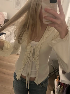 Beige volangtop med knyt från Gina Tricot - Supersöt beige topp från Gina Tricot med volangkant längs v-ringningen och knyt framtill. Tycker denna tröjan är jättefin men säljer för att den inte används så mycket. Perfekt till våren! Jag brukar använda ett linne under med de funkar utan också!