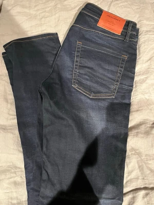 Mörkblå jeans från Jack & Jones - Snygga mörkblå jeans från Jack & Jones med klassisk femficksdesign och kontrastsömmar. Jeansen har en rak passform och är tillverkade i ett mjukt denimtyg som ger en skön känsla. Perfekta för en avslappnad och stilren look.