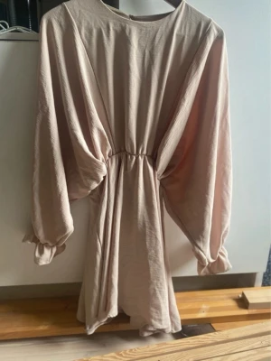 Beige kortklänning med vida ärmar - Säljer en beige kortklänning med markerad midja och vida, långa ärmar med resår vid handlederna. Den är verkligen super fin, men passar inte riktigt mig som är en blek fis. Använd endast en gång! 