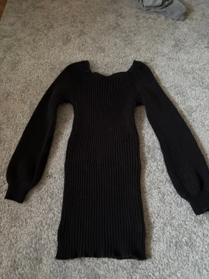 Svart ribbad stickad klänning - Säljer en svart stickad klänning med ribbad struktur. Klänningen har långa ärmar och en kroppsnära passform som framhäver siluetten. Perfekt för dig som gillar en enkel men snygg look. Materialet känns mjukt och stretchigt. Perfekt till en sen sommarkväll🌸☀️