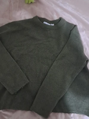 Olivgrön stickad tröja öager 157 - Mysig olivgrön stickad tröja från lager 157 med rund halsringning och långa ärmar. Tröjan har en enkel och avslappnad passform, perfekt att slänga på sig när det är kyligt ute. Materialet känns mjukt och skönt mot huden.