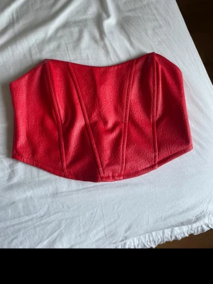 Röd korsett topp från Nelly - Snygg röd korsett topp från Nelly i strukturmönstrat tyg. Toppen har markerade sömmar framtill och dragkedja bak.