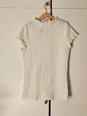 Vit full length topp - Säljer en vit ribbad topp med korta ärmar och lätt fransade kanter. Toppen har en enkel, rak passform och är tillverkad i ett mjukt, stretchigt material.