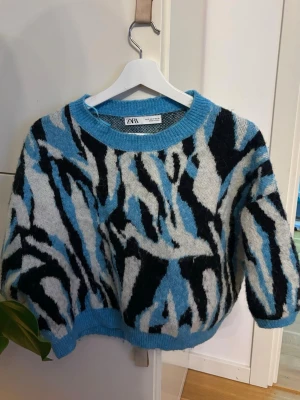 Blå och svart mönstrad stickad tröja Zara - Cool stickad tröja från Zara med blå, svart och vit abstrakt mönster. Tröjan har rund halsringning, ribbade muddar och en avslappnad passform. 