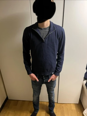Mörkblå halvzip tröja från junkyard - Mörkblå tröja från junkyard med halv dragkedja vid halsen. Tröjan har långa ärmar, ribbade muddar och en avslappnad passform. Perfekt för lager på lager och enkel att matcha med jeans eller chinos. Tröjan är S men skulle säga att den passar XS bättre.