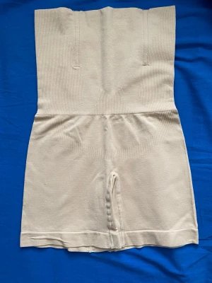 Beige shapewear med hög midja - Säljer ett par beige shapewear shorts med extra hög midja för smickrande siluett. Sömlös design och stretchigt material som formar midja och höfter. Perfekt under klänningar eller kjolar för en slät look. Materialet känns mjukt och följsamt.
