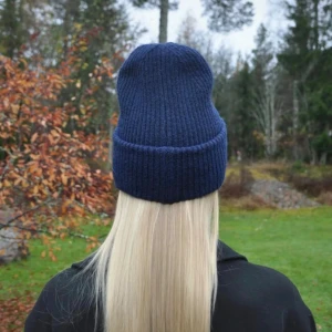 Mörkblå satinmössa - Snygg mörkblå ribbstickad mössa med uppvikt kant och slät, glansig insida i satinliknande material. Perfekt för dig som vill ha en stilren och enkel look med extra komfort. Passar till de flesta outfits och håller dig varm under kalla dagar.