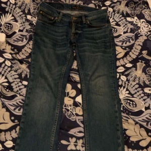Blå raka jeans från nudie - Klassiska blå jeans från nudie med rak passform och fem fickor. Jeansen har en snygg tvättad look och kontrastsömmar. Perfekta för en avslappnad stil och tillverkade i slitstarkt denimtyg.