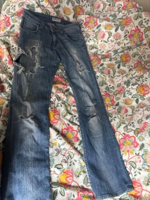 Blå slitna jeans med hål - Säljer ett par blå jeans med slitningar och hål. Dom är väldigt lågmidjade och är bootcut/ lite baggy. Dom är i fint skick! Säljer för dom var för små💞