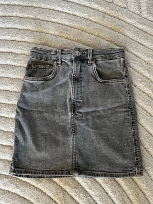 Grå jeanskjol från Zara - Säljer en klassisk grå jeanskjol i kort modell. Kjolen har en rak passform och är tillverkad i slitstarkt denimtyg. Perfekt att matcha med en t-shirt eller hoodie för en avslappnad look.